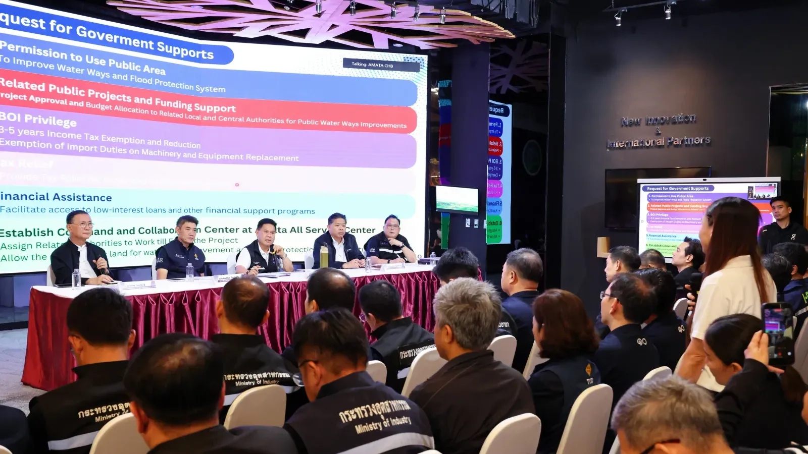 การประชุมรับฟังผู้ประกอบการที่ได้รับผลกระทบจากน้ำท่วม ณ นิคมอุตสาหกรรมอมตะซิตี้ ชลบุรี เมื่อ 8 ตุลาคม 2026 บนจอแสดงรายการข้อเรียกร้องต่อภาครัฐ Request for Government Supports