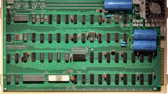 แผงวงจร Apple-1 ปี 1976 สีเขียว มีตัวเก็บประจุสีน้ำเงิน ชิป 6502 ตัวถังเซรามิกสีขาว และข้อความ Apple Computer 1 ที่จัดแสดงใน National Museum of American History ภาพประกอบเรื่องประมูล Apple-1
