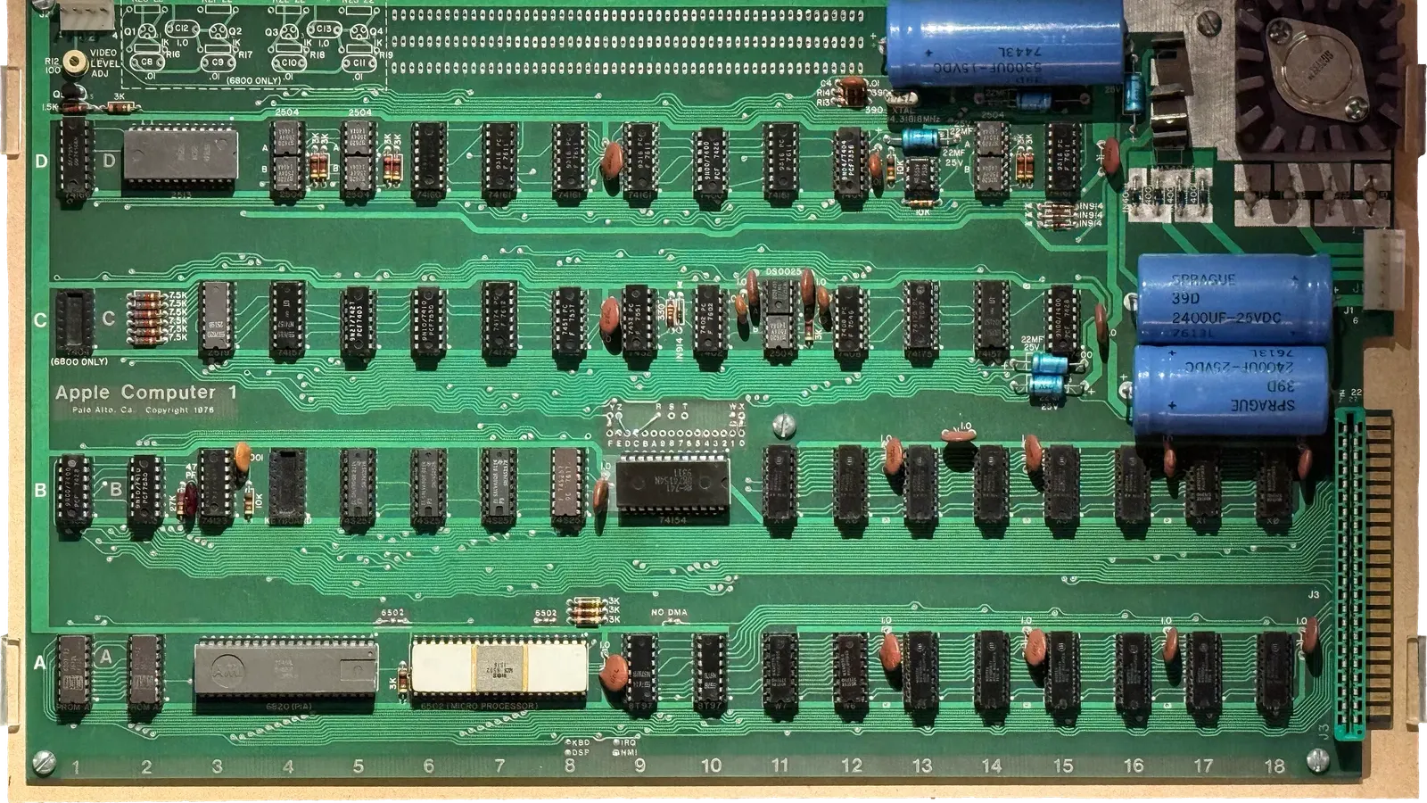 แผงวงจร Apple-1 ปี 1976 สีเขียว มีตัวเก็บประจุสีน้ำเงิน ชิป 6502 ตัวถังเซรามิกสีขาว และข้อความ Apple Computer 1 ที่จัดแสดงใน National Museum of American History ภาพประกอบเรื่องประมูล Apple-1