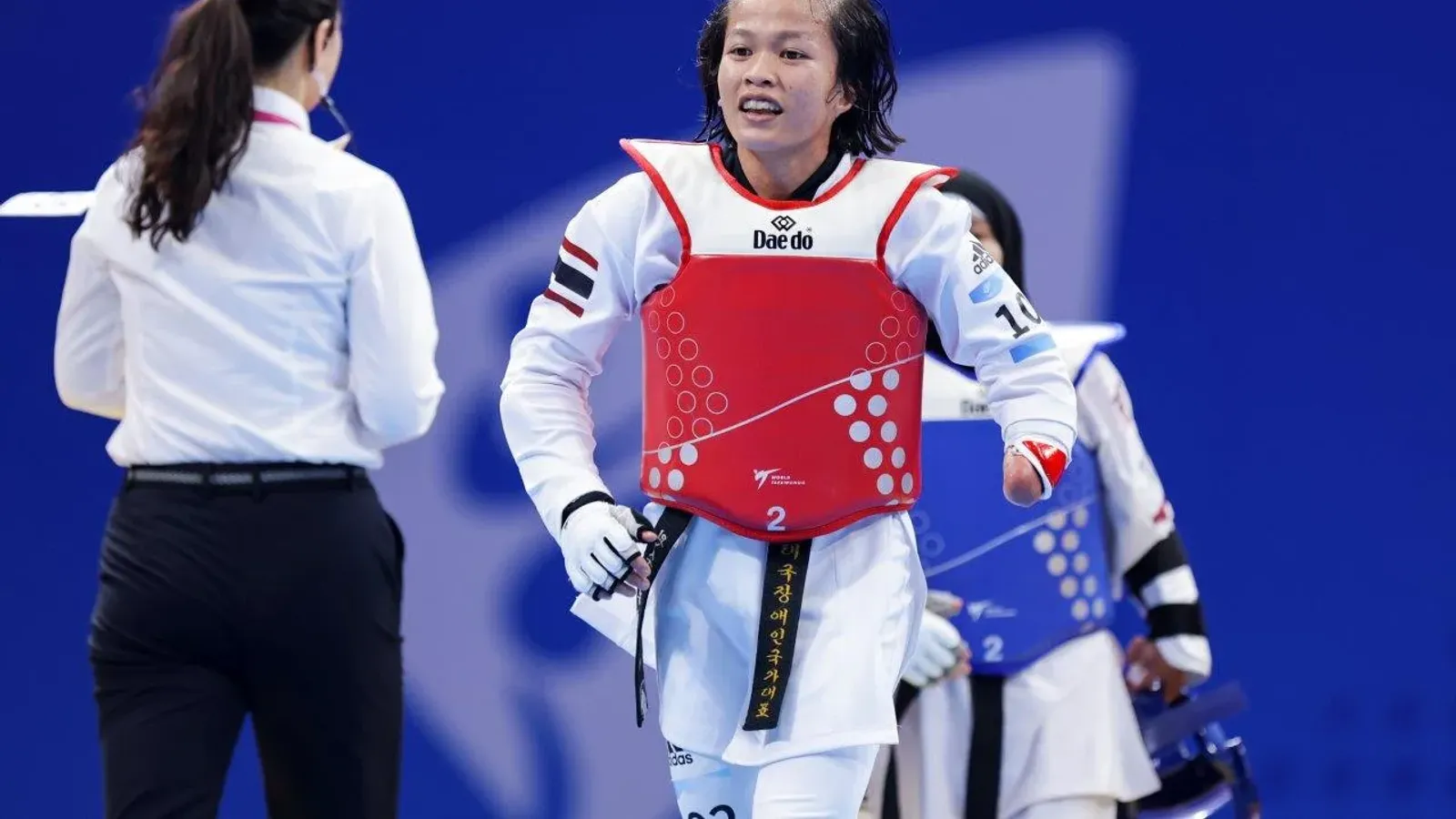 Khwansuda Phuangkitcha นักพาราเทควันโดทีมชาติไทย ผู้ได้เหรียญเงินในตารางเหรียญเอเชียนพาราเกมส์ 2026 สวมชุดเทควันโดสีขาว เกราะป้องกันลำตัวสีแดง และสายดำ เดินบนสนามแข่งข้างกรรมการ