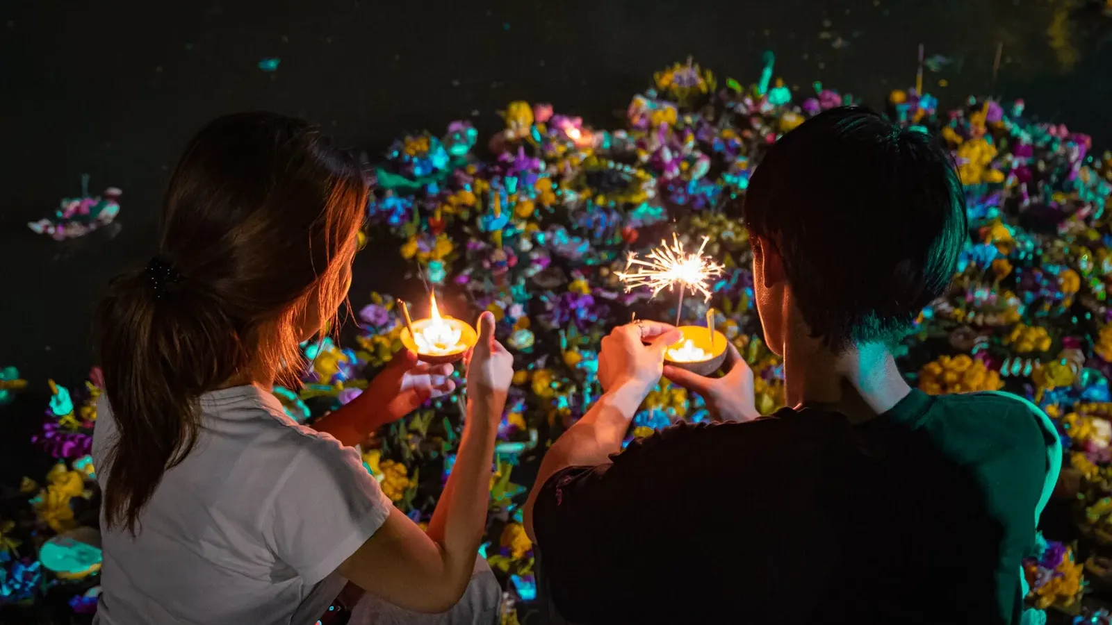 คนสองคนวางกระทงจุดเทียนลงบนผิวน้ำ ภาพประกอบลอยกระทง 2569 กทม. 5 จุด