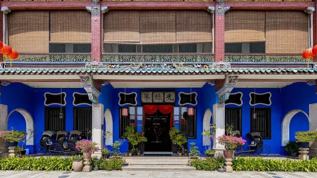 ด้านหน้า Blue Mansion ปีนัง หรือคฤหาสน์ Cheong Fatt Tze ผนังสีคราม ระเบียงชั้นสองมีราวเหล็กหล่อ และไม้กระถางเรียงหน้าบ้าน ภาพถ่ายเดือนมกราคม 2020