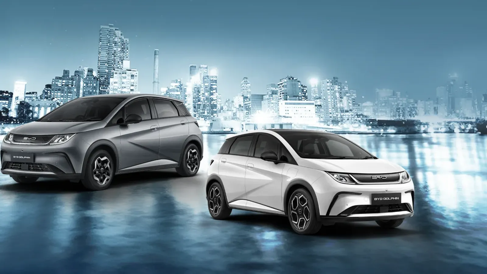 BYD DOLPHIN สองคัน สีเทาและสีขาว จอดหน้าฉากเมืองยามค่ำคืน