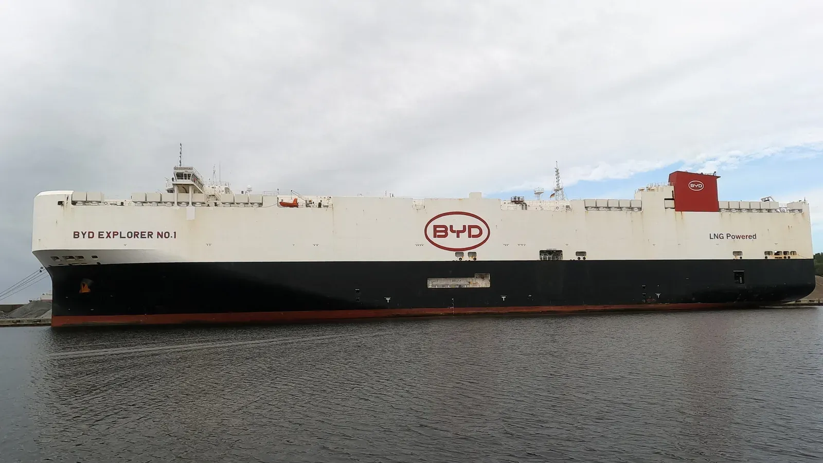 เรือขนส่งรถยนต์ BYD EXPLORER NO.1 ของ BYD จอดเทียบท่าที่ Wilhelmshaven ประเทศเยอรมนี ตัวเรือสีขาวมีโลโก้ BYD และข้อความ LNG Powered