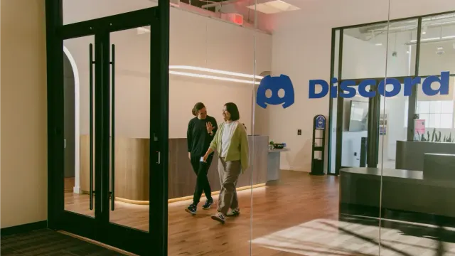 พนักงานสองคนเดินในสำนักงาน Discord ที่มีโลโก้บริษัทบนผนัง