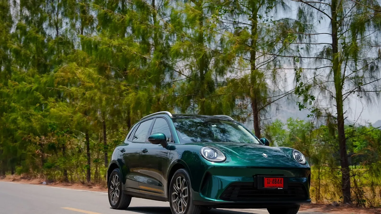 GWM ORA 5 EV สีเขียวเข้ม ป้ายแดงไทย แล่นบนถนนที่มีต้นไม้สองข้าง