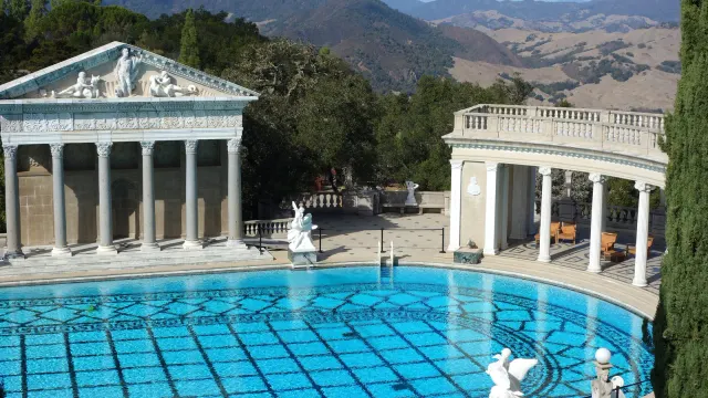 Neptune Pool ของ Hearst Castle สระกลางแจ้งพื้นกระเบื้องลาย หน้าวิหารแบบกรีก-โรมันที่ปลายสระ แนวเสาโค้ง และเทือกเขาด้านหลัง