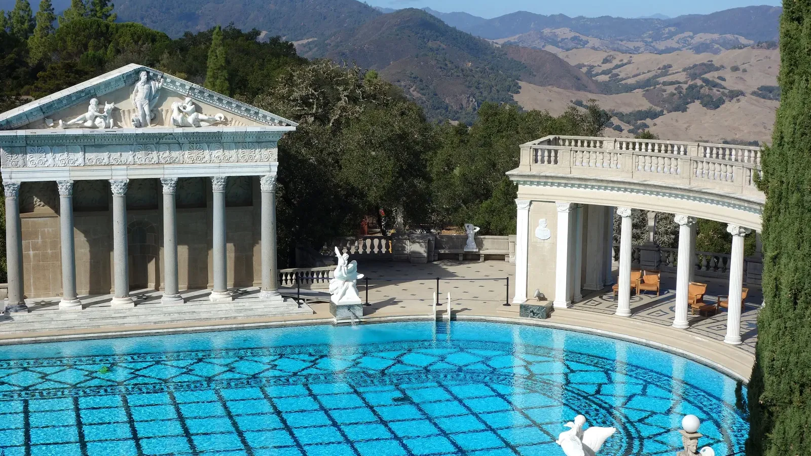 Neptune Pool ของ Hearst Castle สระกลางแจ้งพื้นกระเบื้องลาย หน้าวิหารแบบกรีก-โรมันที่ปลายสระ แนวเสาโค้ง และเทือกเขาด้านหลัง