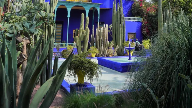 อดีตสตูดิโอสีน้ำเงินเข้มของ Jacques Majorelle กลาง Jardin Majorelle ระเบียงชั้นบน กระบองเพชรสูง และแอ่งน้ำด้านหน้า
