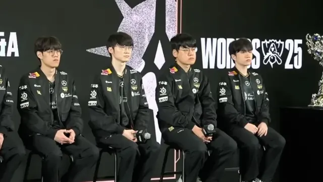 ผู้เล่นทีม T1 แชมป์เก่าในเสื้อแข่งสีดำนั่งบนเวทีงาน Media Day ของ Worlds 2025 ข้างถ้วยรางวัลแชมป์โลก ก่อนป้องกันแชมป์ใน LoL Worlds 2026 เวลาไทย