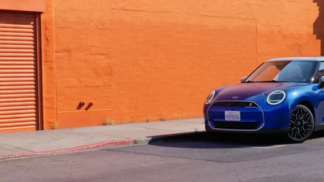 MINI Cooper SE ไฟฟ้าสีน้ำเงินหลังคาขาว จอดริมถนนหน้ากำแพงสีส้ม ภาพจากหน้ารุ่น Cooper ไฟฟ้าของ MINI ประเทศไทย