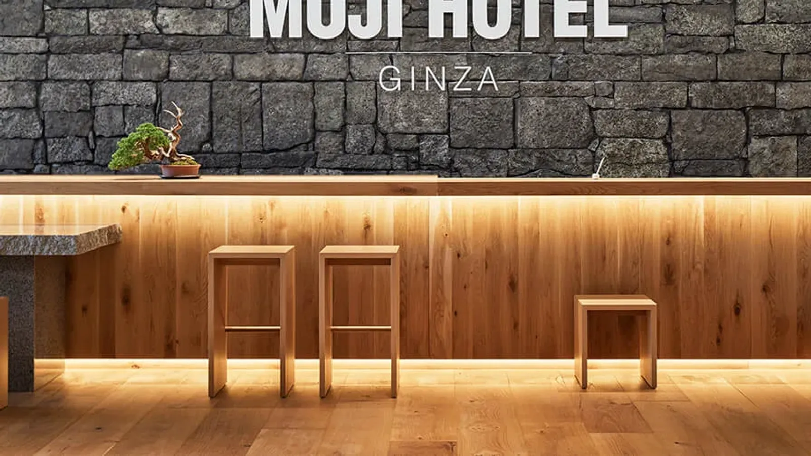 ผนังหินและเคาน์เตอร์ไม้ มีตัวอักษร MUJI HOTEL GINZA ภายในโรงแรมของแบรนด์ MUJI ในโตเกียว
