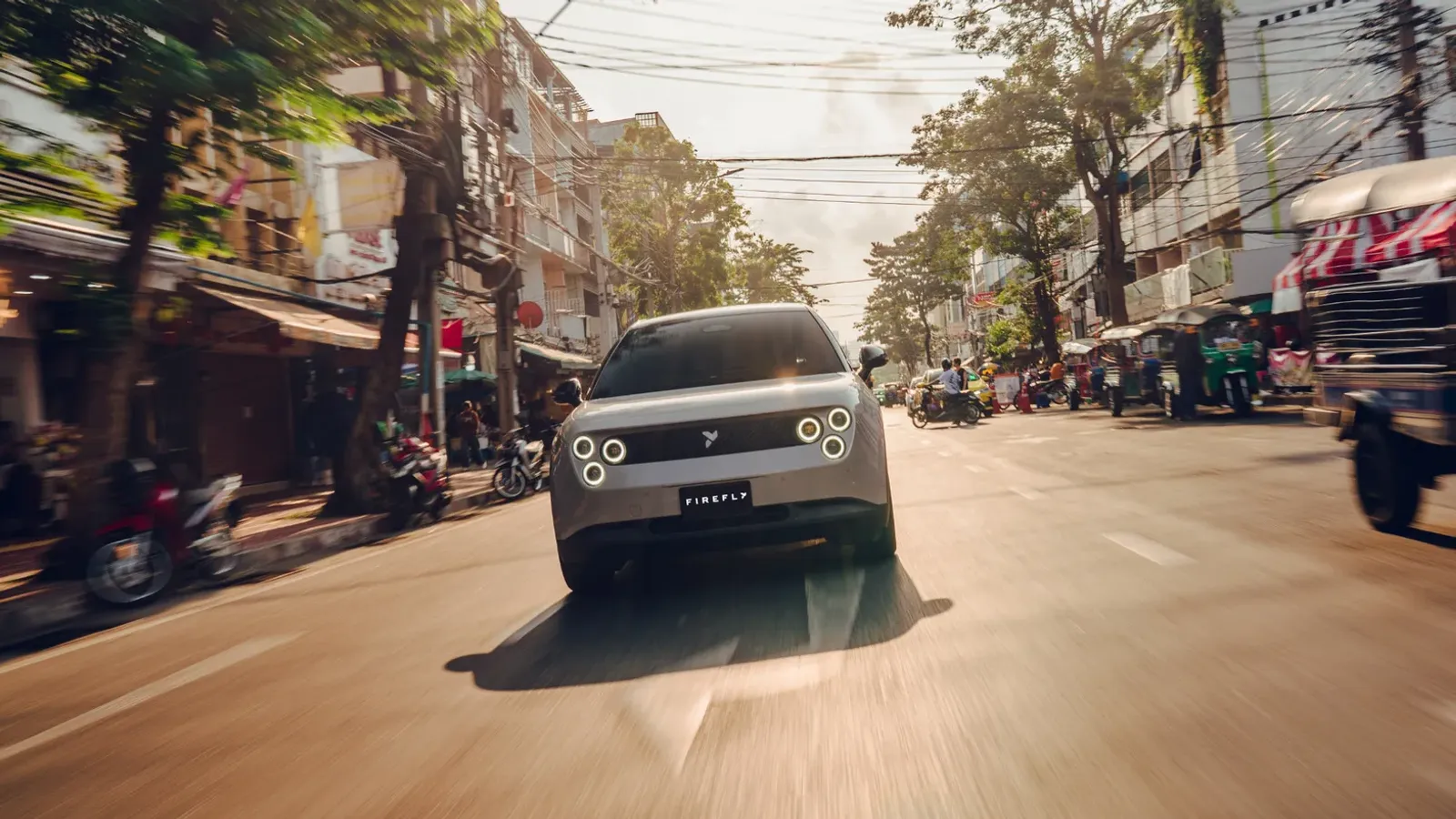 รถยนต์ไฟฟ้า NIO firefly สีเงินวิ่งบนถนนในเมืองที่มีร้านค้าและรถจักรยานยนต์สองข้างทาง ภาพจากเว็บไซต์ firefly ประเทศไทย