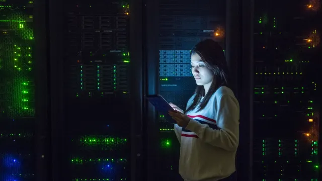 ภาพประกอบประกาศ SecNumCloud ของ Orange: ผู้หญิงถือแท็บเล็ตยืนอยู่ระหว่างตู้แร็กเซิร์ฟเวอร์ในศูนย์ข้อมูล