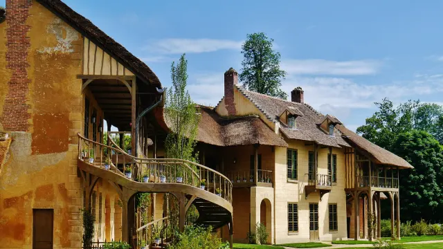 Maison de la Reine และบ้านบิลเลียดใน Hameau de la Reine ของ Petit Trianon ผนังปูนสีเหลืองอ่อน โครงไม้ หลังคามุงฟาง และบันไดวนภายนอก