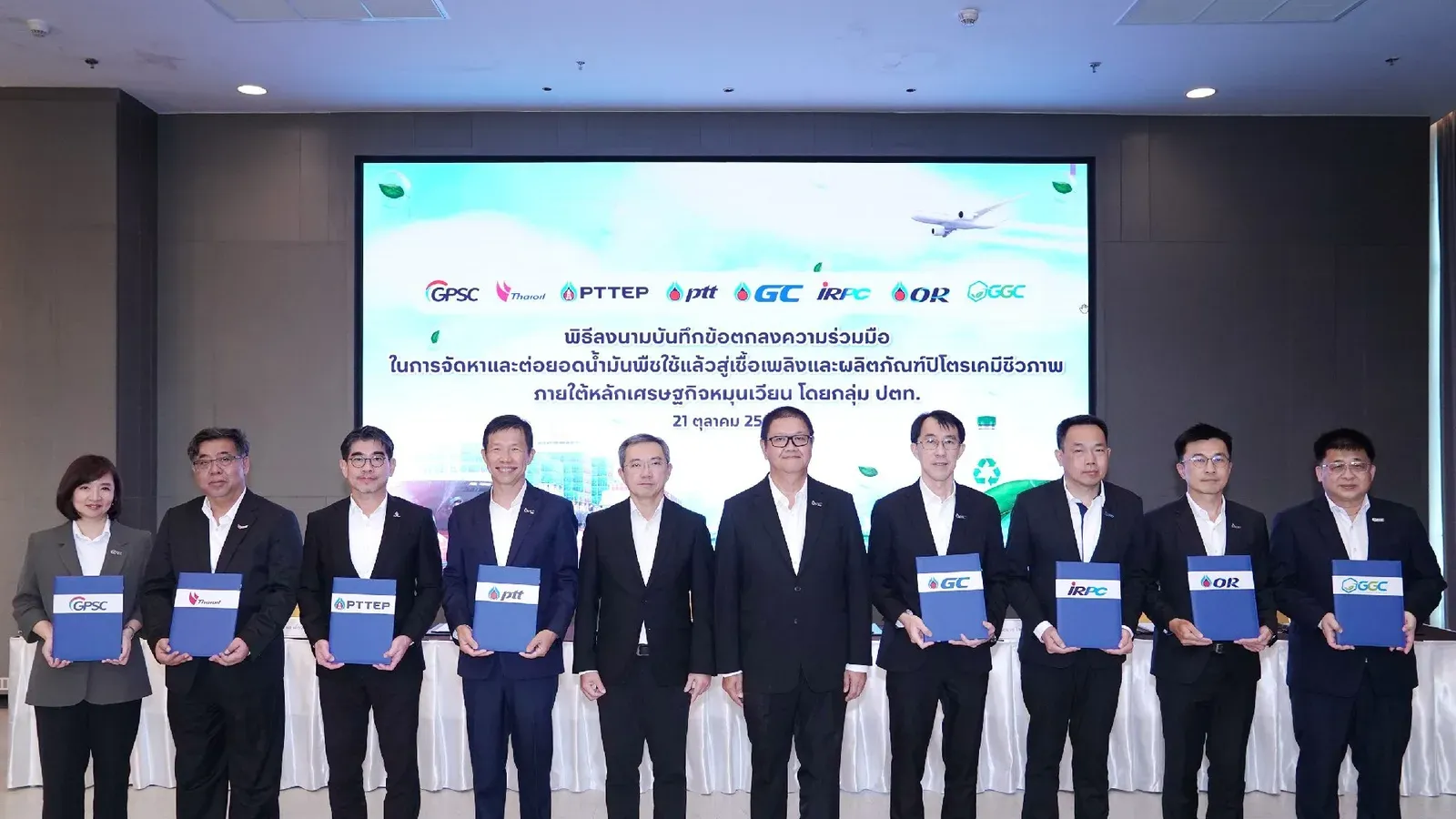 ผู้บริหาร 8 บริษัทกลุ่ม ปตท. ยืนถือแฟ้มบันทึกข้อตกลงความร่วมมือเรื่องน้ำมันพืชใช้แล้ว SAF และปิโตรเคมีชีวภาพ หน้าจอโลโก้ GPSC PTTEP ptt GC IRPC OR และ GGC