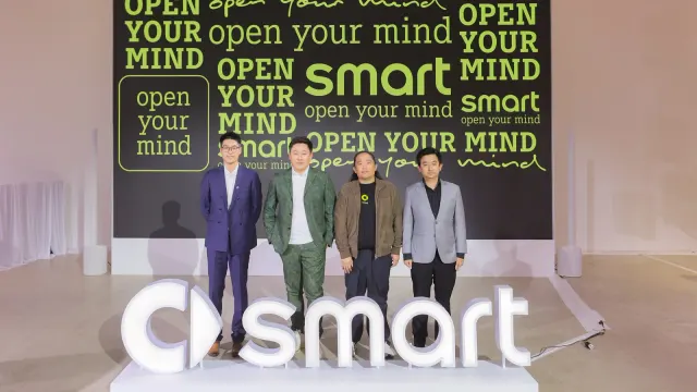 ผู้บริหารยืนบนเวทีงาน smart เปิดตัวในไทยร่วมกับ Thonburi Group หน้าฉากข้อความ open your mind และโลโก้ smart