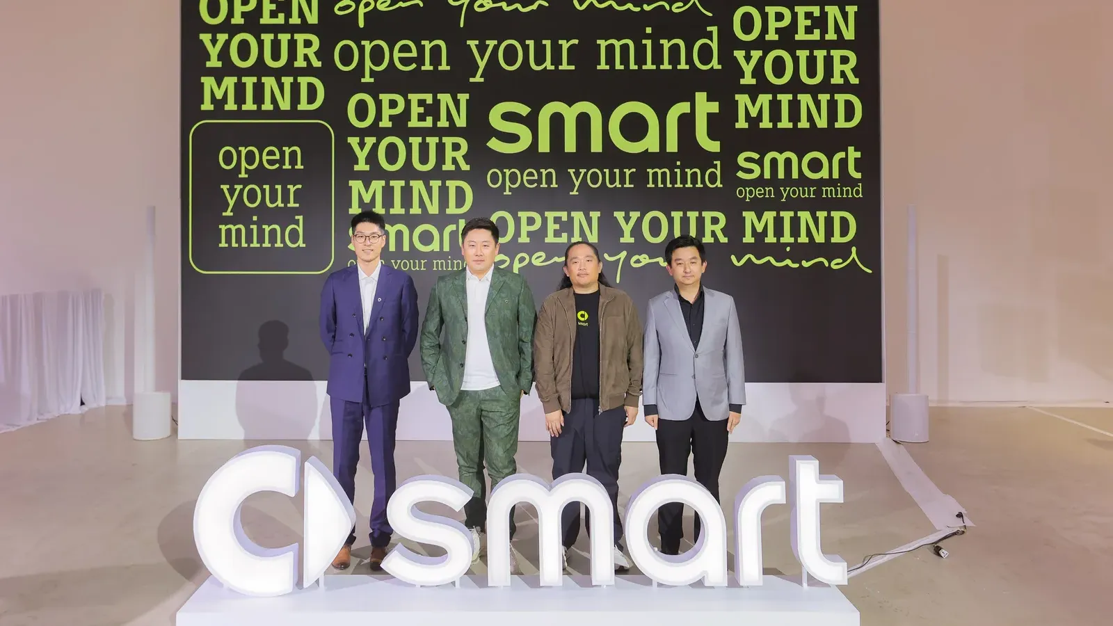 ผู้บริหารยืนบนเวทีงาน smart เปิดตัวในไทยร่วมกับ Thonburi Group หน้าฉากข้อความ open your mind และโลโก้ smart