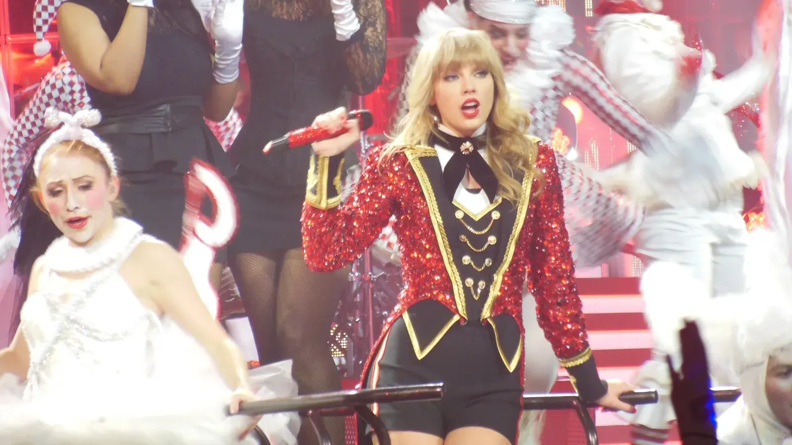 Taylor Swift ในแจ็กเก็ตเลื่อมสีแดงกลางนักเต้นบนเวที The Red Tour ปี 2013 ทัวร์ของอัลบั้ม Red ซึ่งเป็นบ้านแรกของ All Too Well