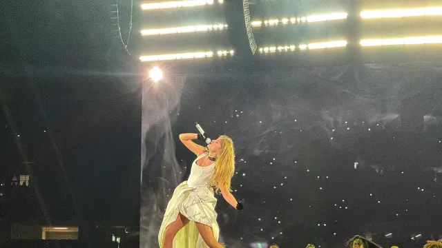 Taylor Swift ในชุดสีขาวของช่วง The Tortured Poets Department ร้องเพลงบนเวที The Eras Tour ที่นิวออร์ลีนส์ 26 ตุลาคม 2024 มีนักเต้นในชุดสีขาวอยู่ด้านขวา