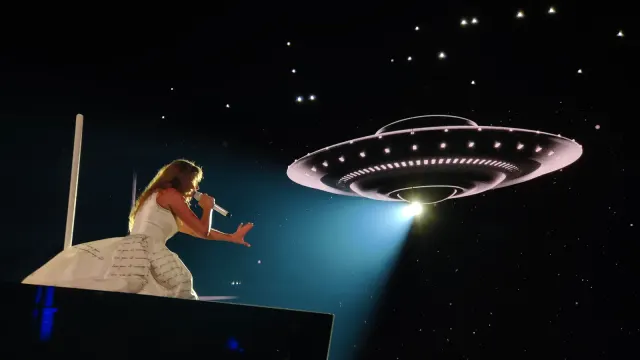 Taylor Swift ในชุดสีขาวร้องเพลงบนเวทีช่วงอัลบั้ม The Tortured Poets Department ของคอนเสิร์ต The Eras Tour ที่ Paris La Défense Arena 11 พฤษภาคม 2024 โดยมีภาพยานอวกาศบนจอด้านหลัง