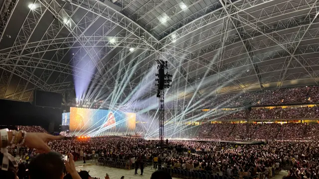 ผู้ชมเต็มพื้นสนามและอัฒจันทร์ใต้หลังคาโครงเหล็กของ Singapore National Stadium ในคอนเสิร์ต The Eras Tour ของ Taylor Swift 9 มีนาคม 2024 โดยมีภาพ Swift บนจอยักษ์หลังเวที