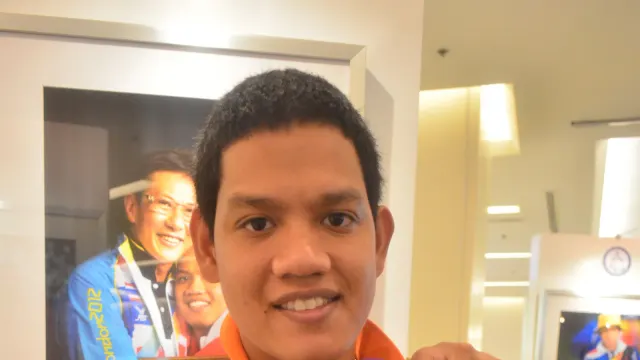Rungroj Thainiyom ในเสื้อโปโลลายทางสีส้มขาว ถือเหรียญทองคล้องริบบิ้นสีม่วง ภาพถ่ายปี 2013