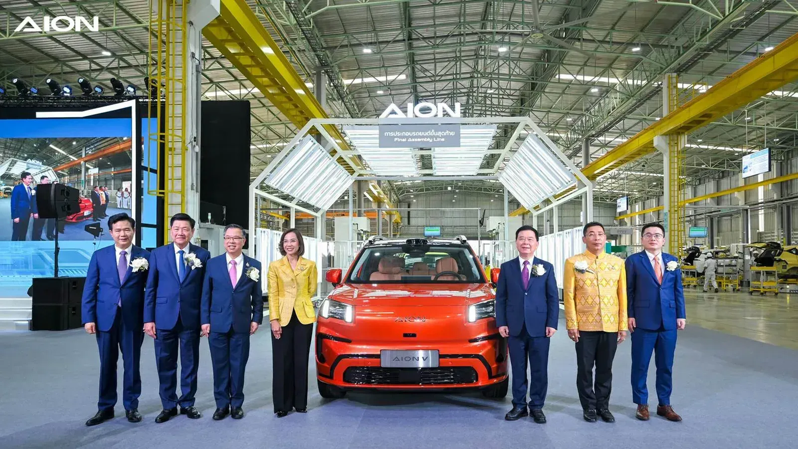 AION V สีส้มจอดหน้าป้ายการประกอบรถยนต์ขั้นสุดท้าย Final Assembly Line ในโรงงาน GAC AION ระยอง โดยมีผู้บริหารยืนสองข้าง