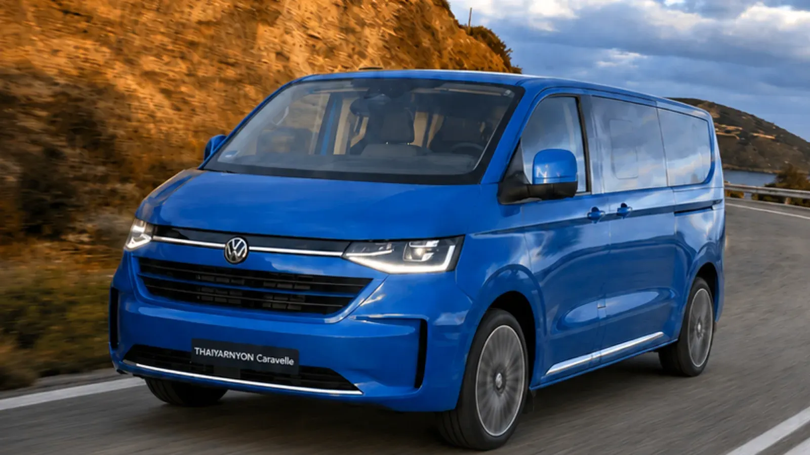 Volkswagen Thaiyarnyon Caravelle T7 สีน้ำเงิน กำลังวิ่งบนถนนเลียบภูเขา ภาพจากโบรชัวร์ทางการของไทยยานยนตร์
