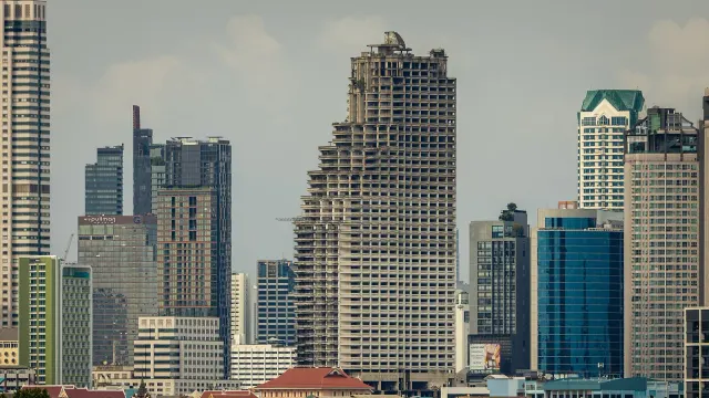 อาคาร Sathorn Unique Tower ในกรุงเทพฯ โครงการคอนโดมิเนียมสูงที่สร้างไม่เสร็จ ซึ่งหยุดก่อสร้างในช่วงวิกฤตต้มยำกุ้ง ตั้งอยู่ท่ามกลางอาคารสูงอื่น ภาพถ่ายภายหลังเมื่อกรกฎาคม 2564