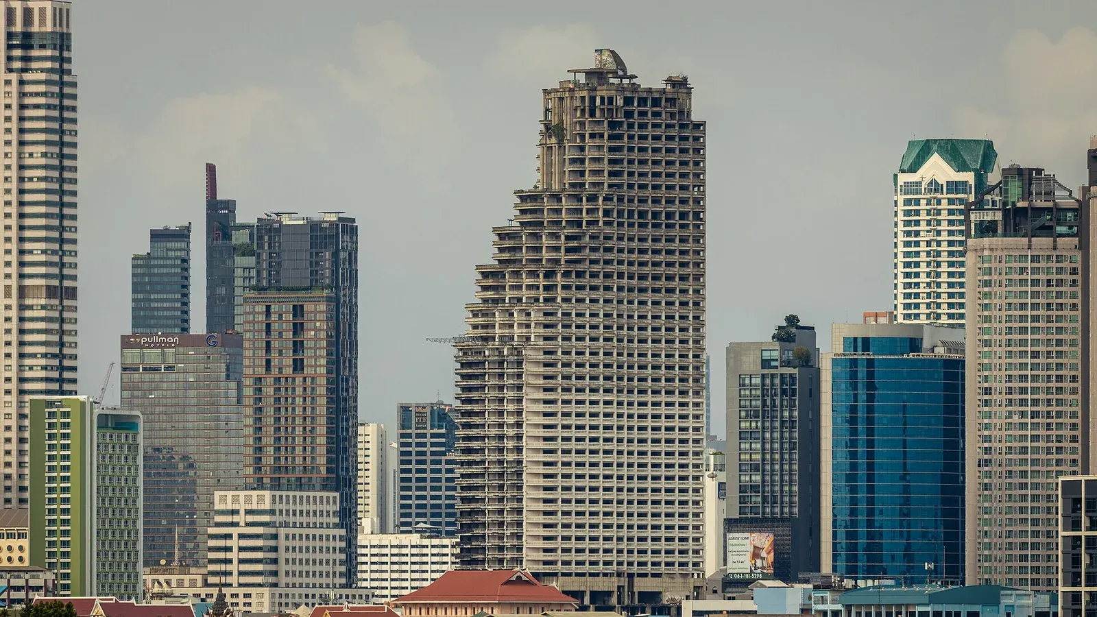 อาคาร Sathorn Unique Tower ในกรุงเทพฯ โครงการคอนโดมิเนียมสูงที่สร้างไม่เสร็จ ซึ่งหยุดก่อสร้างในช่วงวิกฤตต้มยำกุ้ง ตั้งอยู่ท่ามกลางอาคารสูงอื่น ภาพถ่ายภายหลังเมื่อกรกฎาคม 2564