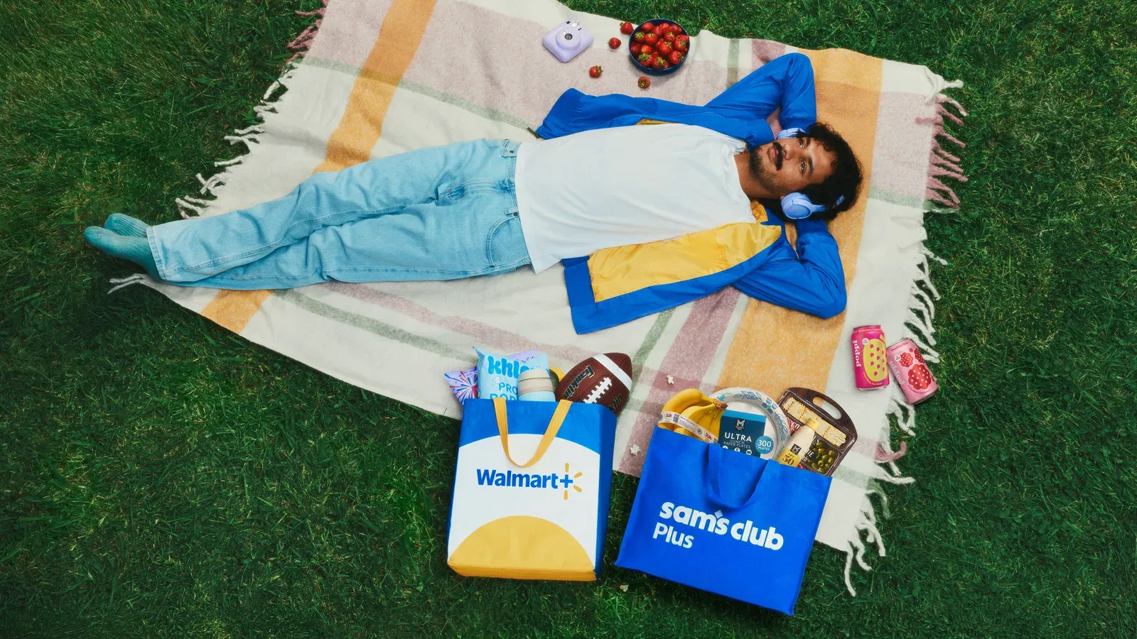 ภาพมุมสูงชายนอนพักบนผ้าปูในสวนสาธารณะ ข้างตัวมีถุงสมาชิก Walmart+ และ Sam's Club Plus ใส่ของกิน