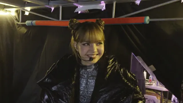 LISA สวมเสื้อคลุมหนังมันสีดำและไมโครโฟนแบบคาดศีรษะ ยิ้มอยู่หลังเวที ภาพแรกอย่างเป็นทางการจากสารคดี Always Lalisa