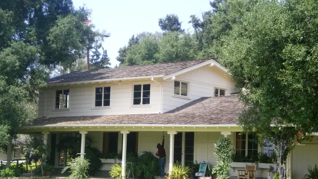 บ้านไร่ใน Will Rogers Ranch ผนังไม้สีขาว หลังคาจั่ว ระเบียงยาวมีเสาไม้ และไม้พุ่มหน้าบ้าน ภาพถ่ายเมื่อพฤษภาคม 2008 ก่อนไฟป่าปี 2025
