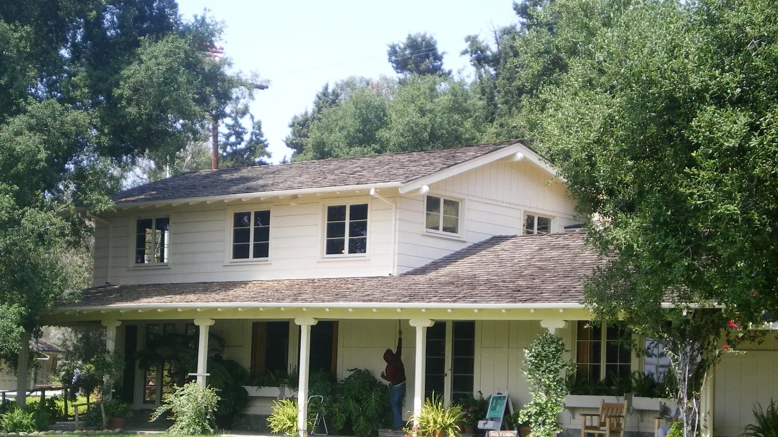 บ้านไร่ใน Will Rogers Ranch ผนังไม้สีขาว หลังคาจั่ว ระเบียงยาวมีเสาไม้ และไม้พุ่มหน้าบ้าน ภาพถ่ายเมื่อพฤษภาคม 2008 ก่อนไฟป่าปี 2025