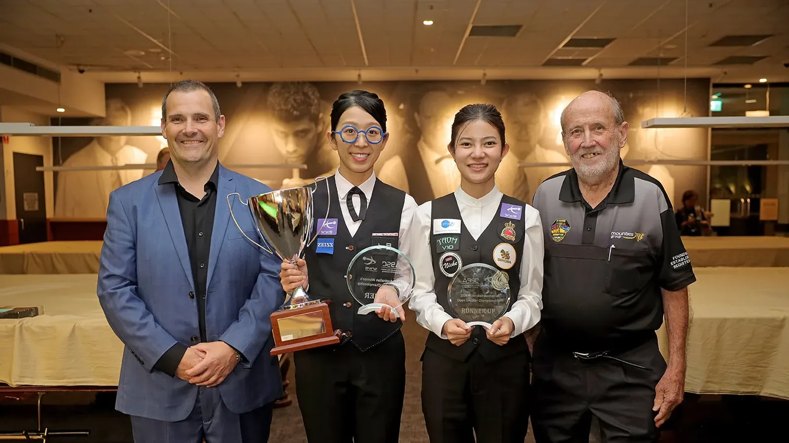 Onyee Ng ถือถ้วยแชมป์และ Mink Nutcharut ถือโล่รองแชมป์สนุกเกอร์หญิง Australian Women's Open 2026 ยืนร่วมกับเจ้าหน้าที่สองคนที่ Mounties ซิดนีย์