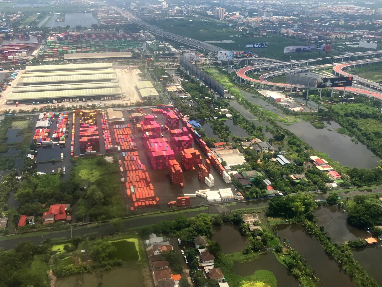 ภาพถ่ายทางอากาศลานตู้คอนเทนเนอร์สีแดงและส้มมีน้ำท่วมขังรอบบริเวณ ลาดกระบัง กรุงเทพฯ