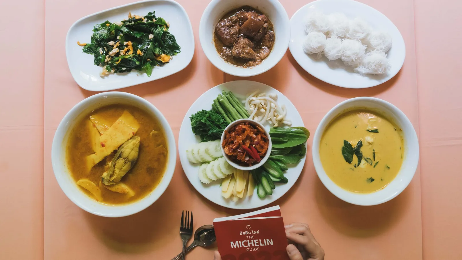 สำรับอาหารไทยหลายจานบนโต๊ะพร้อมเล่มคู่มือมิชลิน ภาพประกอบข่าวรางวัลของ ททท.
