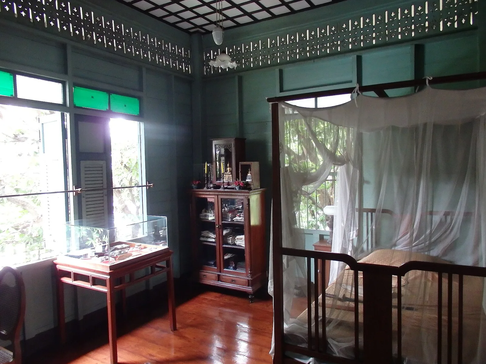 ห้องนอนที่มีช่องลมไม้ฉลุเหนือผนังและเตียงกางมุ้ง ในพิพิธภัณฑ์ชาวบางกอก