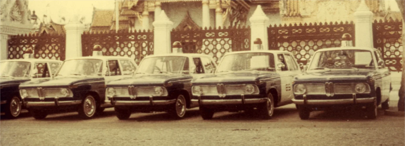 รถ BMW 2000 ติดไฟสัญญาณบนหลังคาห้าคันจอดเรียงแถวหน้ารั้วอาคาร ภาพประกอบปี 2512 (1969) ที่ BMW 2000 เป็นรถยนต์ของตำรวจนครบาล