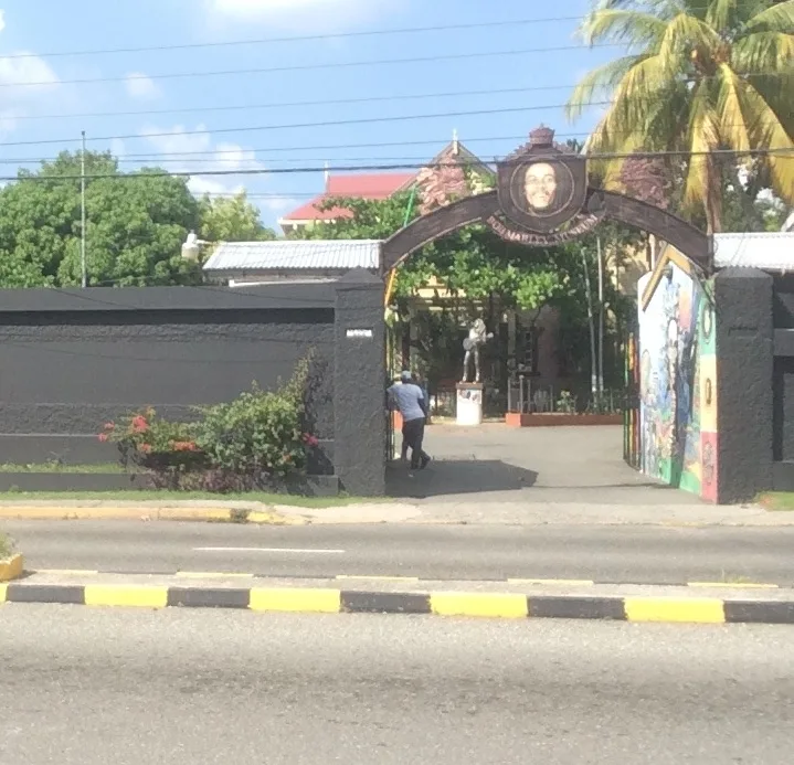 ประตูโค้งหน้า Bob Marley Museum ริมถนน Hope Road มีภาพใบหน้า Bob Marley บนซุ้มประตูและรูปปั้นในลานด้านใน ภาพถ่ายปี 2021
