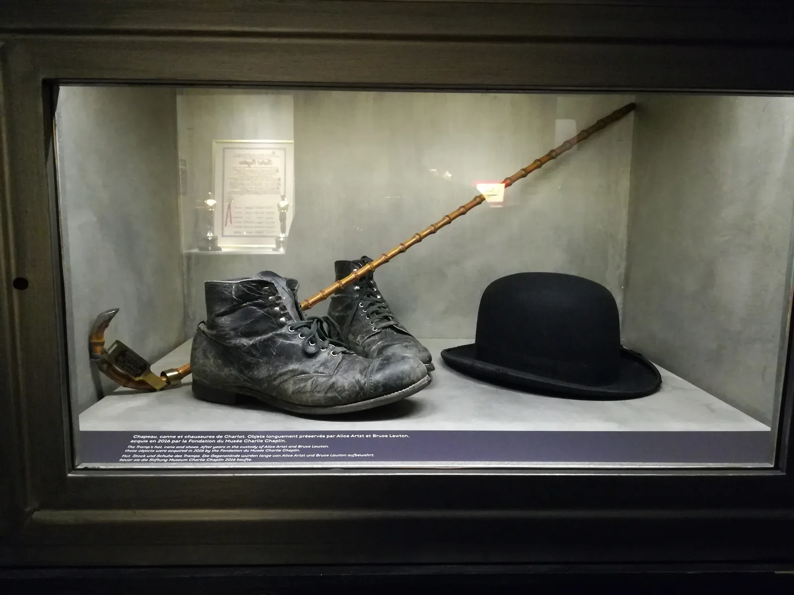 หมวกโบว์เลอร์ ไม้เท้า และรองเท้าของตัวละคร The Tramp ในตู้จัดแสดงที่ Chaplin's World ภาพถ่ายเมื่อ 17 สิงหาคม 2017