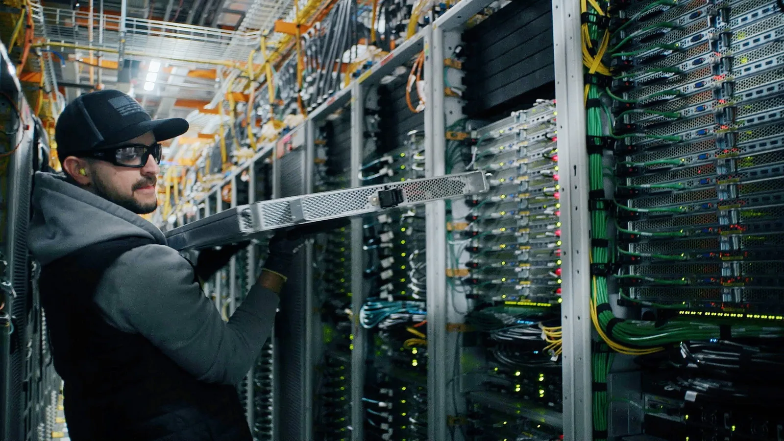 ช่างเทคนิคสวมหมวกแก๊ปและแว่นตานิรภัยทำงานหน้าตู้เซิร์ฟเวอร์ใน AWS