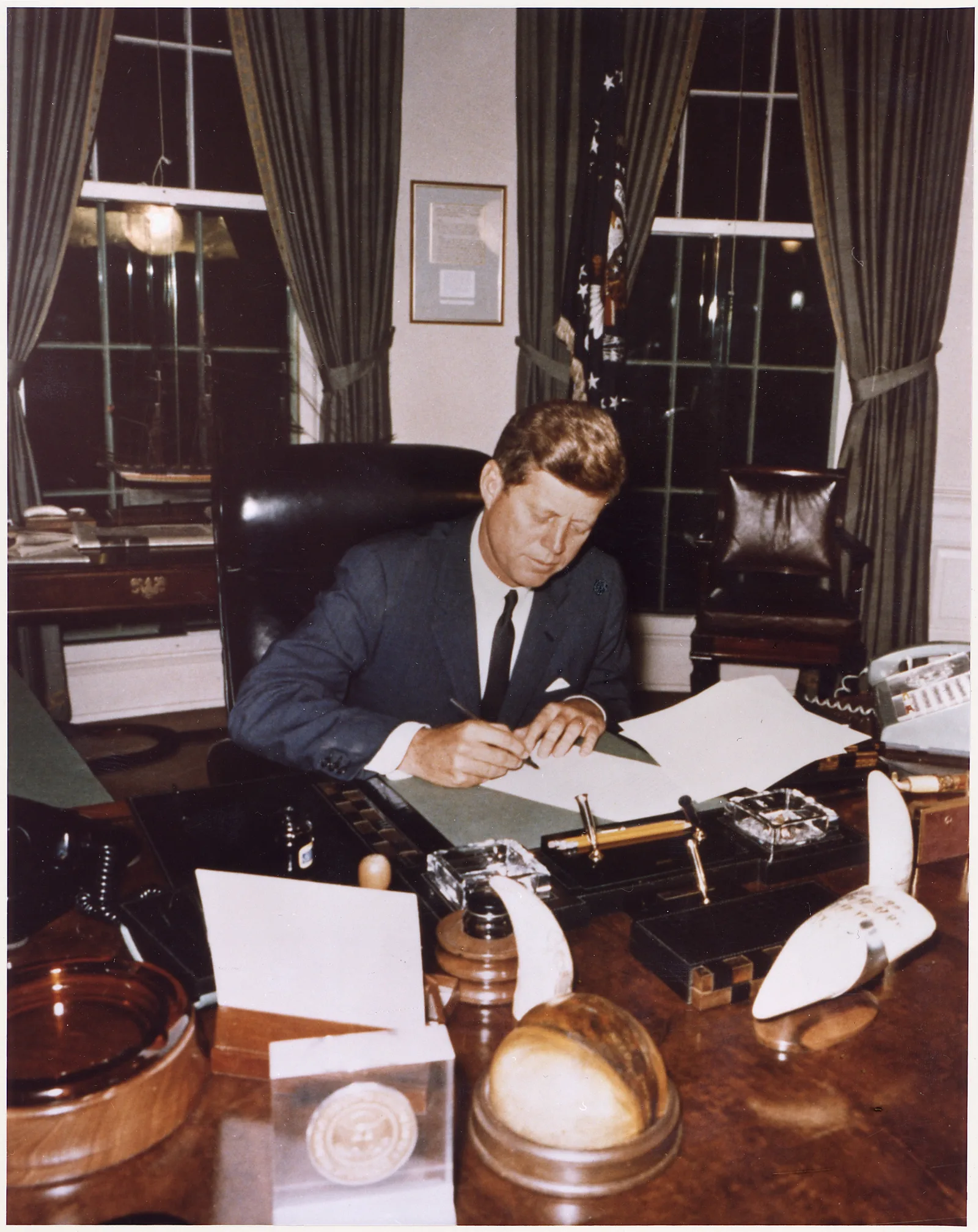 ประธานาธิบดี John F. Kennedy นั่งลงนามเอกสารที่โต๊ะทำงานในห้องทำงานรูปไข่ ทำเนียบขาว เมื่อ 23 ตุลาคม 1962 ซึ่งหอจดหมายเหตุแห่งชาติสหรัฐฯ ระบุว่าเป็นการลงนามประกาศกักกันคิวบา