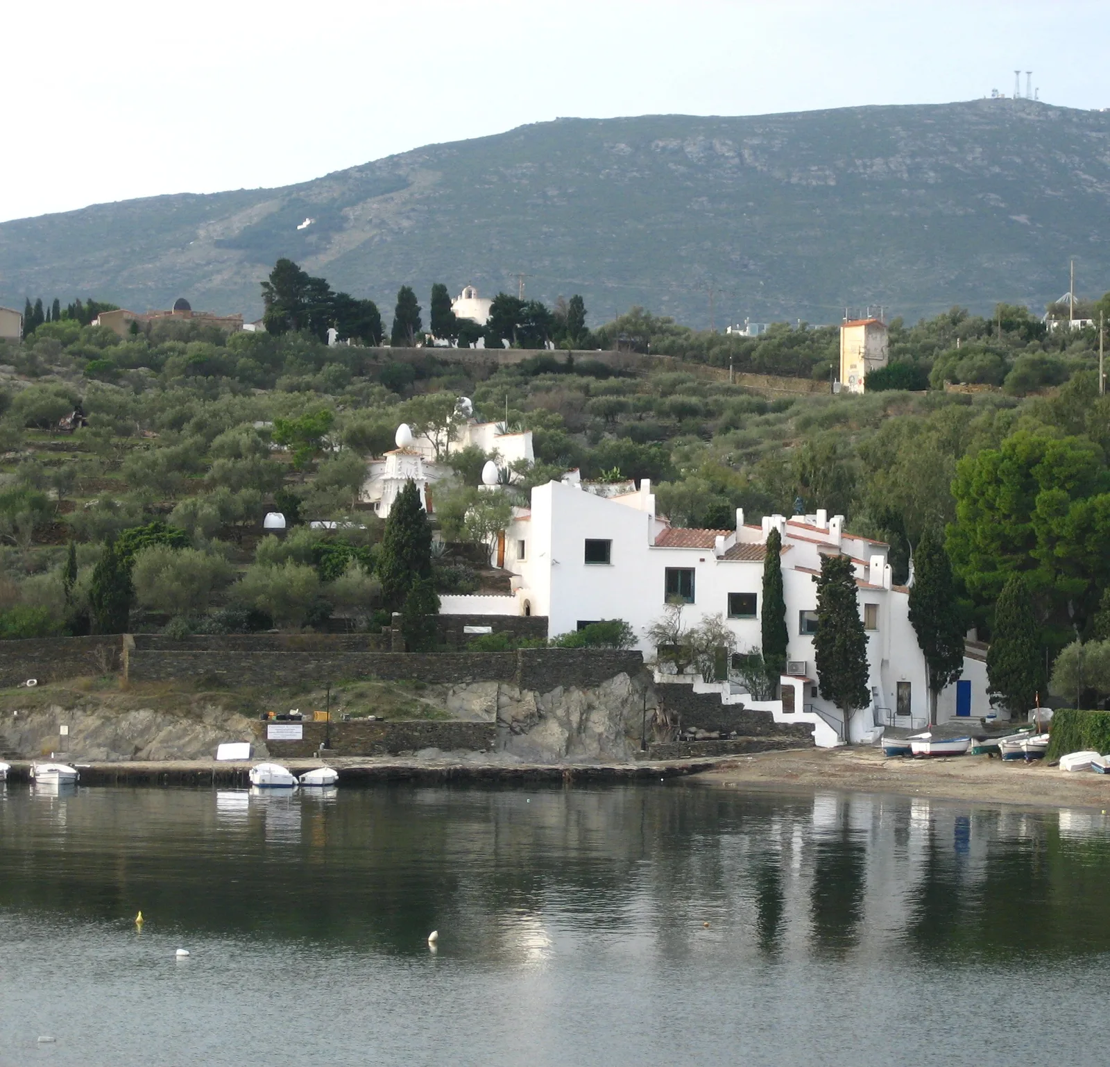 Casa-museu Salvador Dalí ริมอ่าว Portlligat อาคารสีขาวบนเชิงเนินที่มีต้นไม้และขั้นบันได ฉากหลังเป็นภูเขา ภาพถ่ายเดือนธันวาคม 2007 (ครอปภาพ)