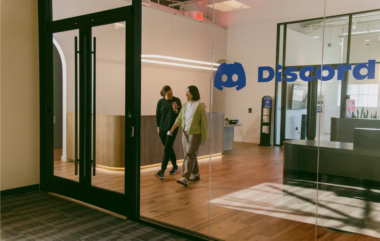 พนักงานสองคนเดินในสำนักงาน Discord ที่มีโลโก้บริษัทบนผนัง