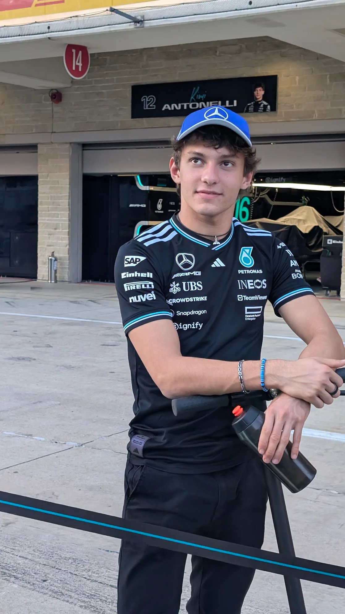 Kimi Antonelli สวมเสื้อทีม Mercedes และหมวกแก๊ปสีน้ำเงิน ยืนหน้าโรงรถหมายเลข 12 ที่สนาม COTA ออสติน ปี 2025