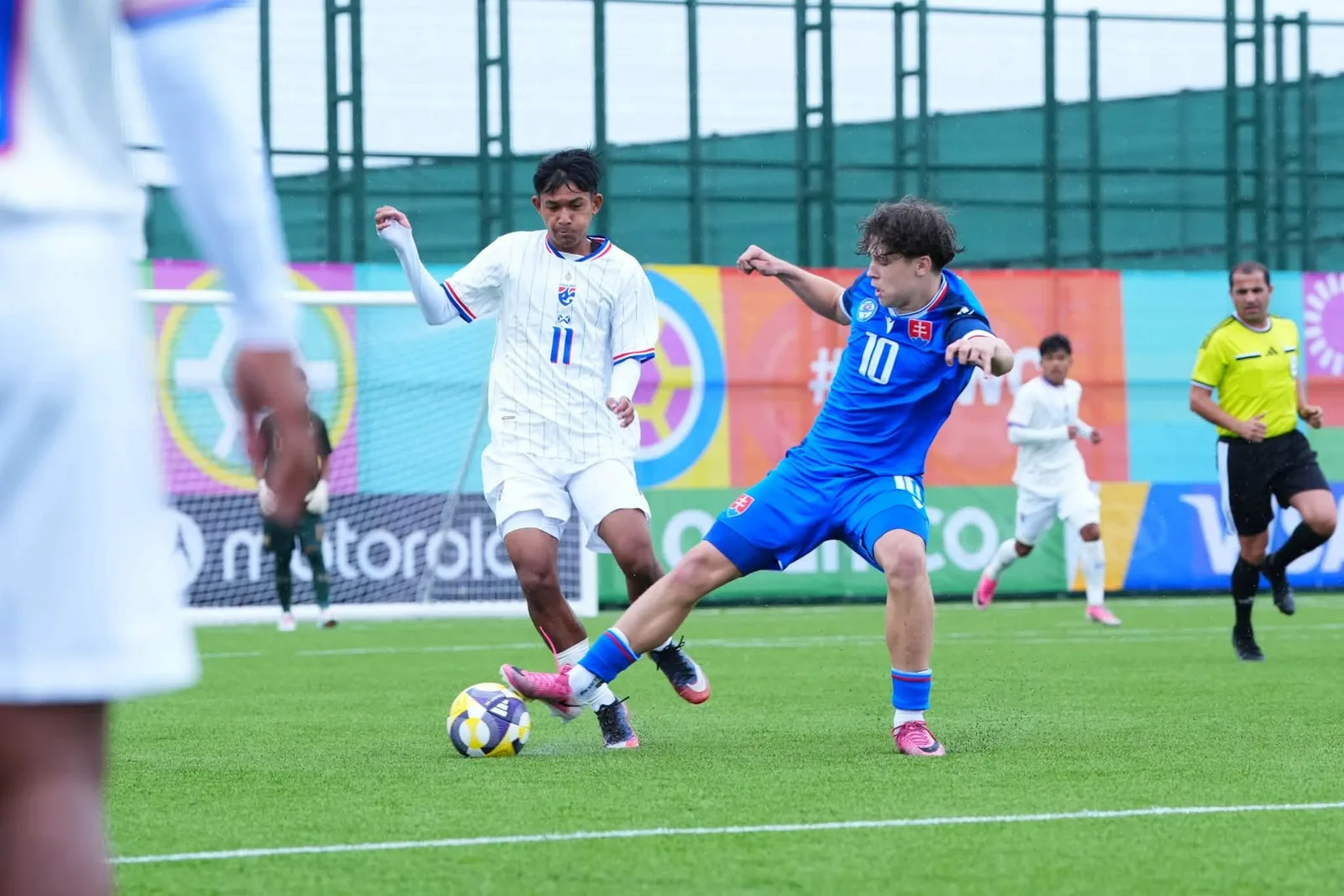 ผู้เล่นทีมชาติไทย U15 หมายเลข 11 ชุดขาว แย่งบอลกับผู้เล่นสโลวาเกียชุดน้ำเงิน ใน FIFA U-15 World Cup 2026 ทีมชาติไทยนัดที่สองที่บากู