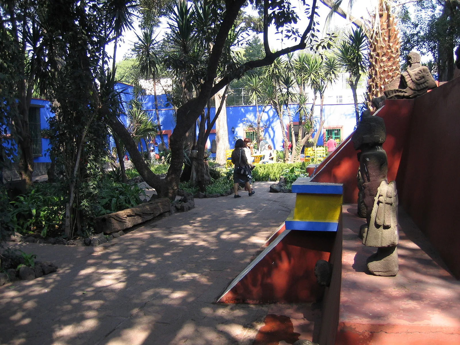 สวนของ Casa Azul บ้านของ Frida Kahlo ทางเดินร่มไม้ใหญ่และต้นปาล์ม ล้อมด้วยผนังสีน้ำเงิน