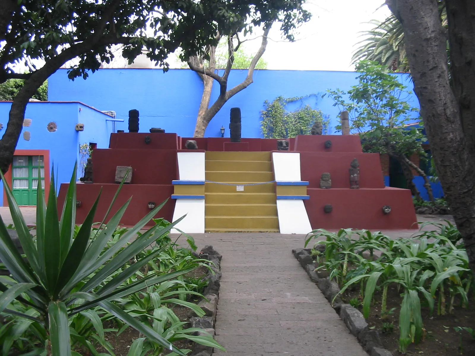 พีระมิดขนาดเล็กในลานสวนของ Casa Azul ทาสีแดง บันไดกลางสีเหลือง ด้านบนวางรูปสลักหิน ภาพถ่ายเดือนมีนาคม 2008